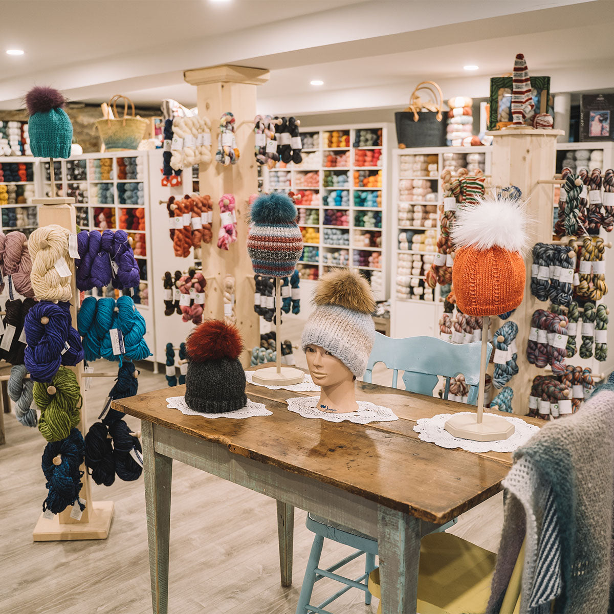 Plusieurs tuques exposées sur une table dans la boutique Phildar café-tricot