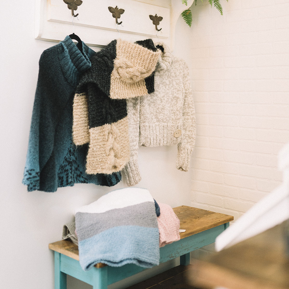 Plusieurs morceaux de vêtement tricotés accrochés au mur de la boutique Phildar café-tricot